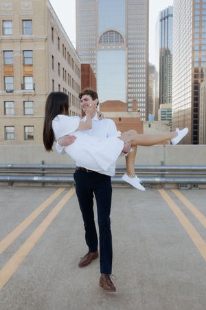 A couple embraces in a romantic moment on an urban rooftop with city buildings in the background.