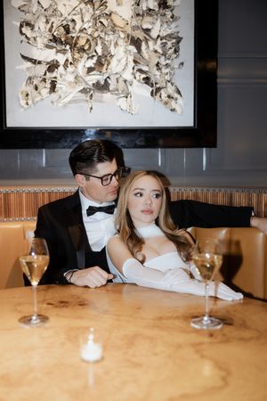 Couple in evening wear seated at a restaurant table beneath modern art decor.