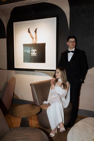 Couple in formal attire posed near Chanel artwork in an upscale lounge setting.