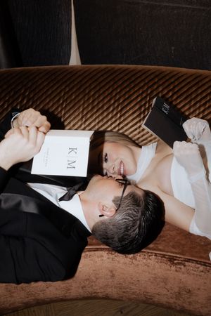 Couple in formal attire lying on brown couch holding menu at upscale venue.
