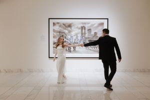 Museum visitors walk through a minimalist white gallery space with framed artwork on the walls.