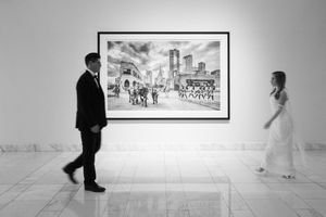 People observe artwork in a bright minimalist gallery with polished floors and framed pieces mounted on white walls.