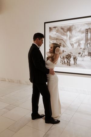 A wedding couple sharing an intimate moment in front of a black and white framed artwork in a bright room.