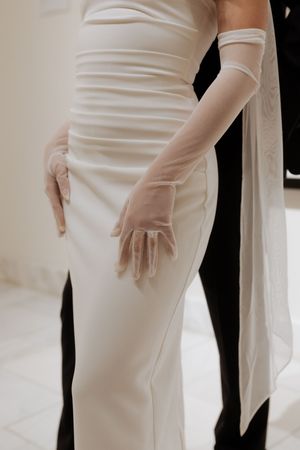 Close-up detail of elegant white wedding dress and sheer gloves.