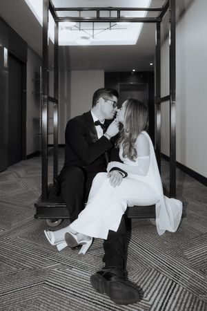 A black and white photo captures an intimate moment between a couple in formal wear in a modern hallway.