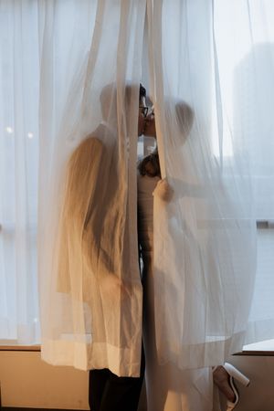 Artistic silhouette of couple behind sheer white curtains creates romantic mood.