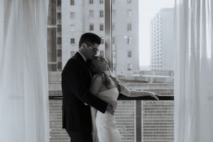 Intimate black and white portrait of couple by window in urban setting.