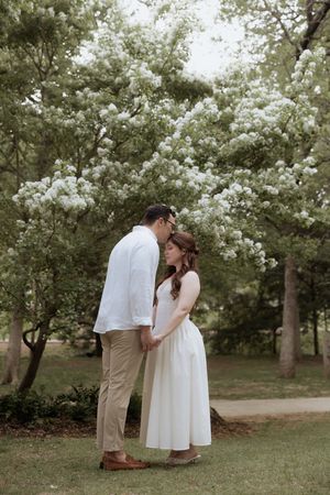 A couple shares a tender moment under blooming white spring trees in a peaceful garden setting.