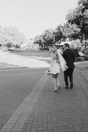 A couple in formal attire walking together on a brick pathway in black and white photography.