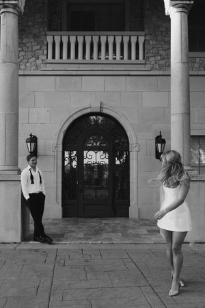 Black and white sequence showing figures walking and dancing across a white stone portico with arched doorways.
