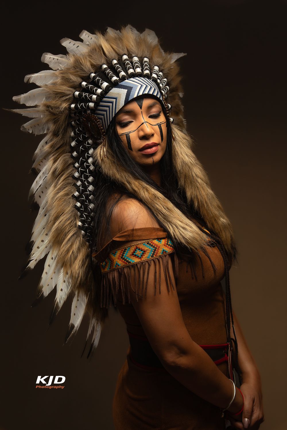 Artistic portrait featuring traditional Native American headdress and brown fringed dress against dark background.