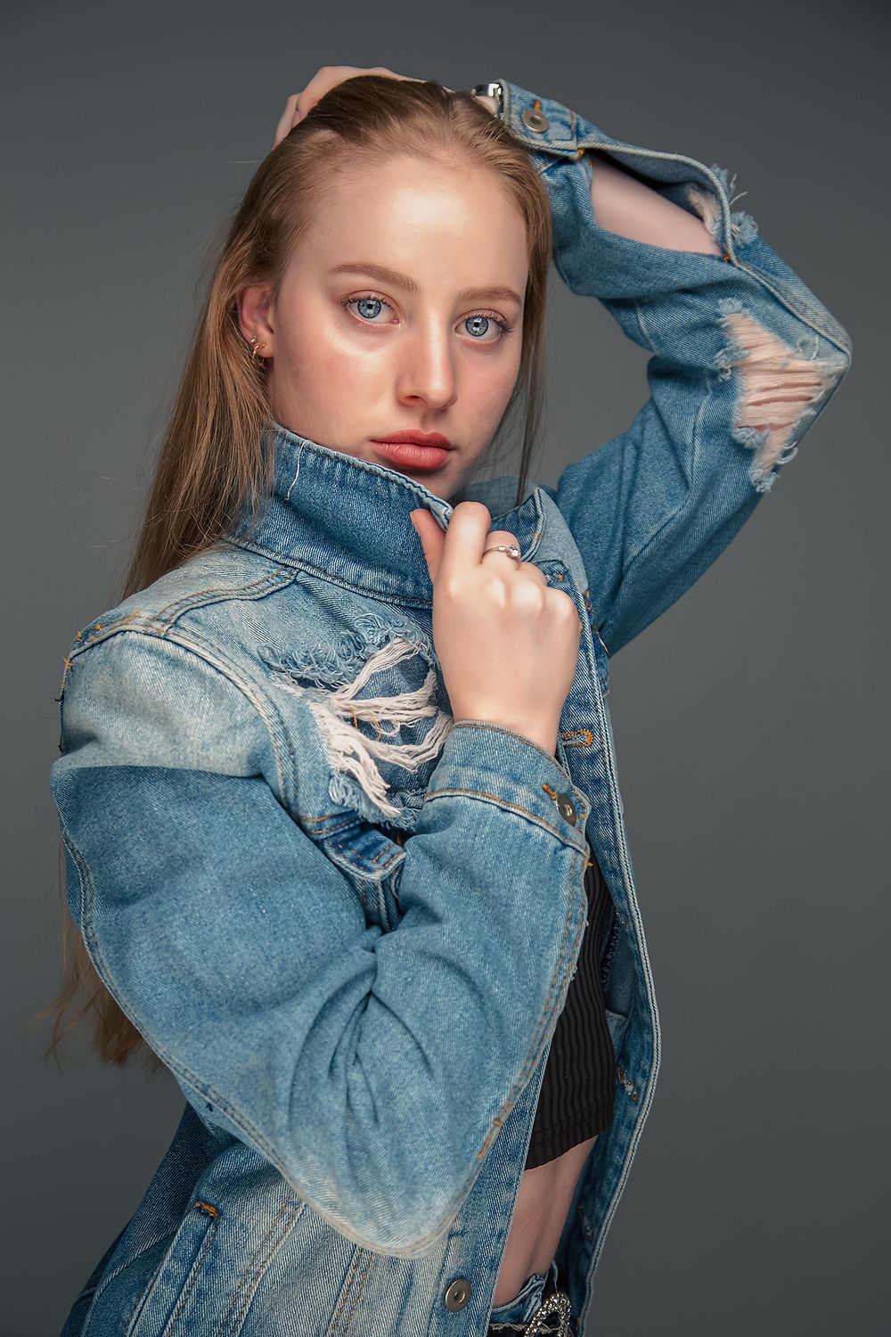Fashion portrait featuring an oversized distressed denim jacket against a dark studio backdrop.