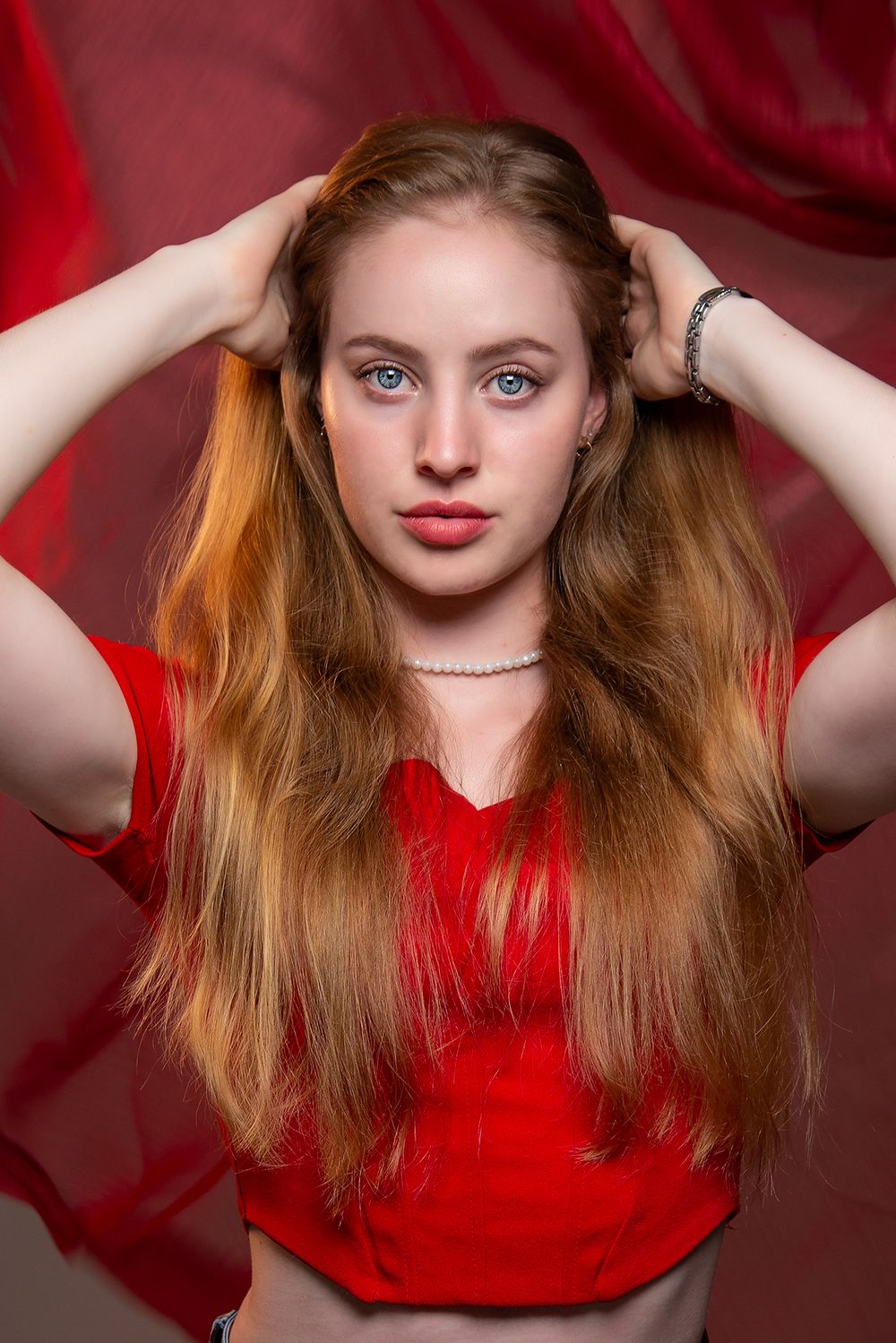 Four similar artistic portrait shots of someone with red hair wearing a red top against a deep red background.