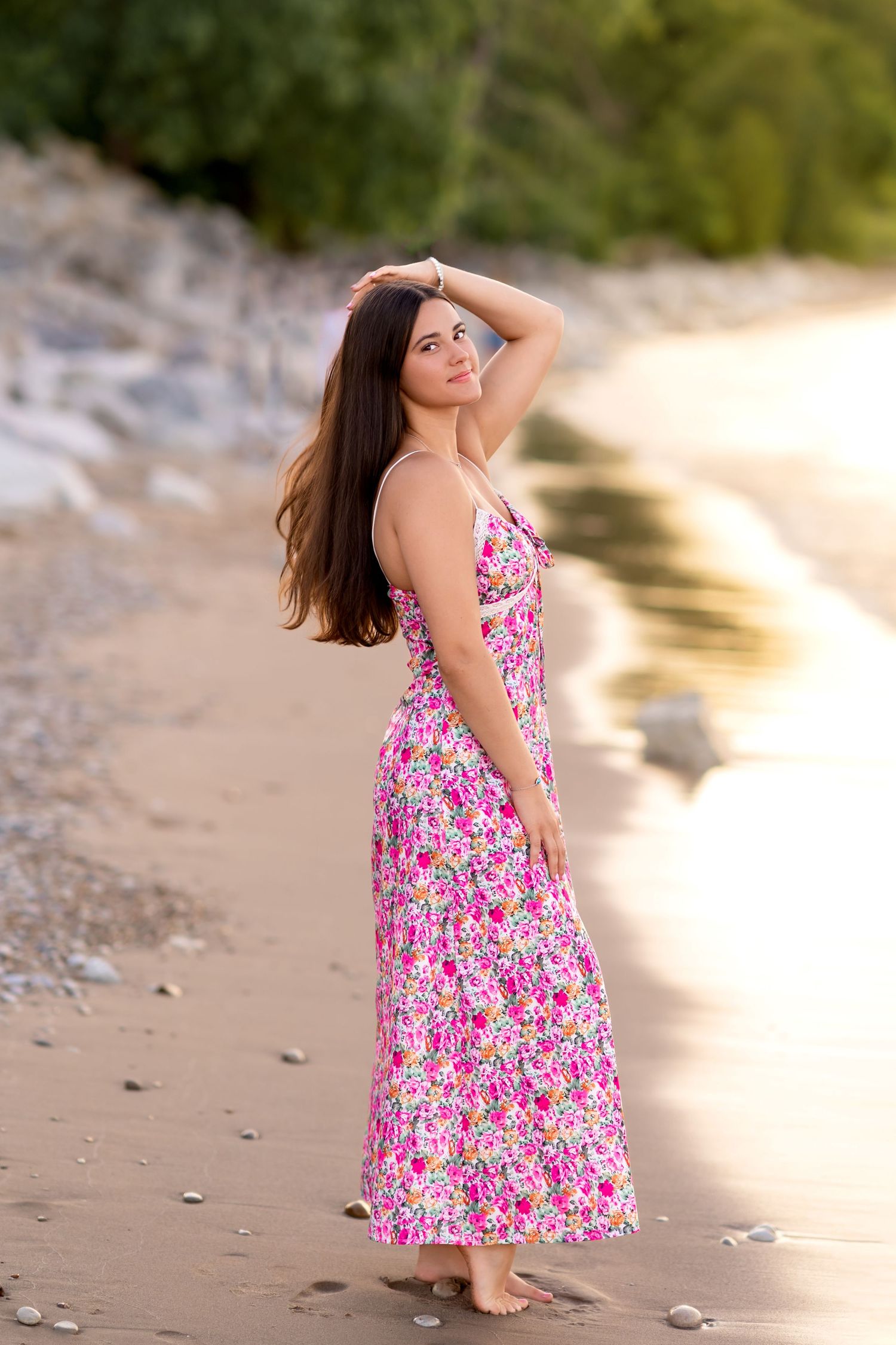 A sandy beach scene at sunset with someone posing in a flowing pink floral summer dress.