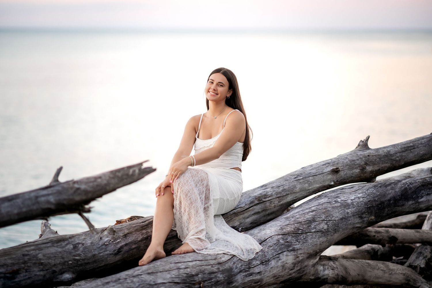 Artistic photo series taken on driftwood at golden hour showing ethereal seaside poses in white.