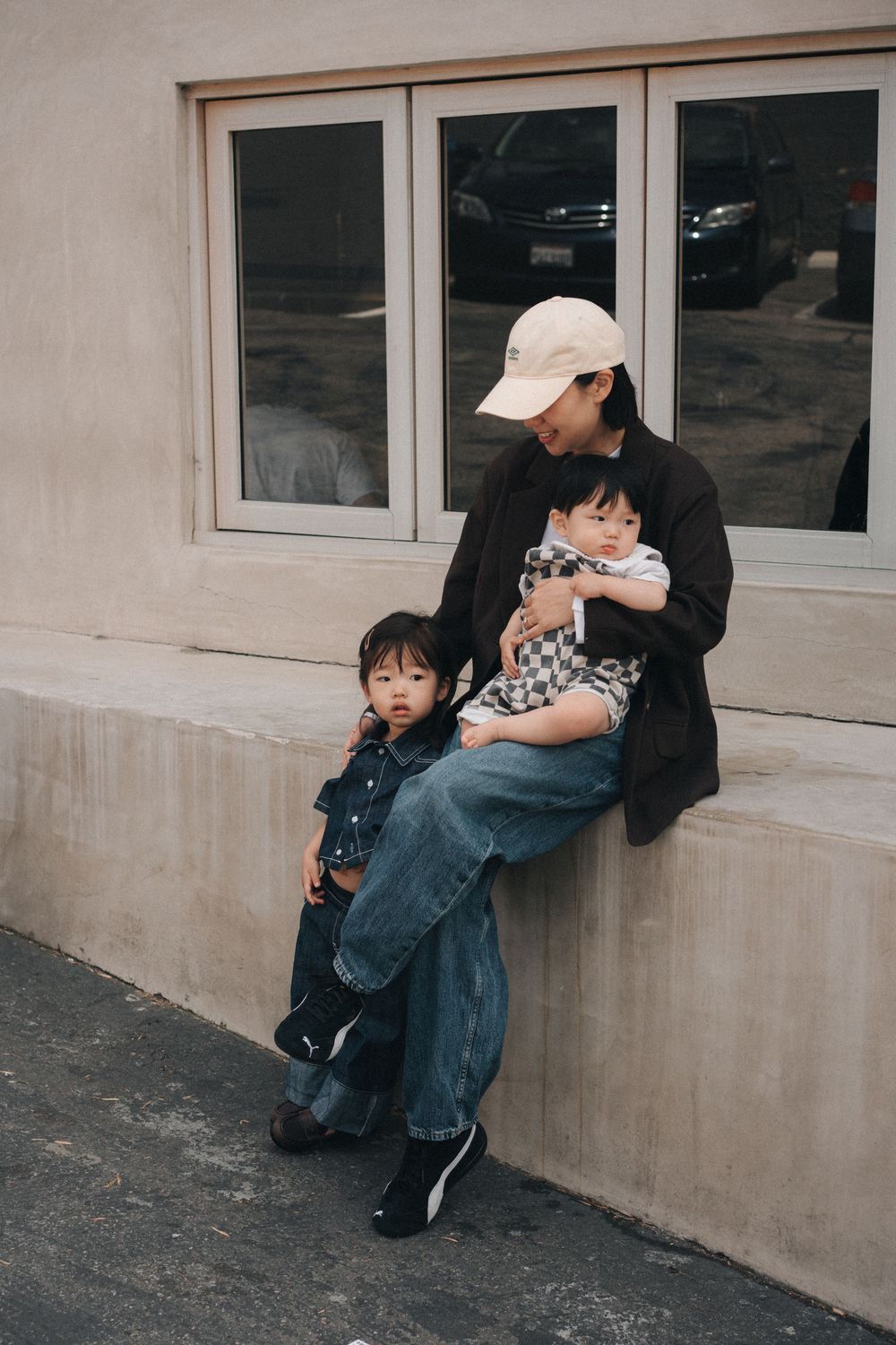 A group sits together on a concrete ledge outside a building with windows on an overcast day.
