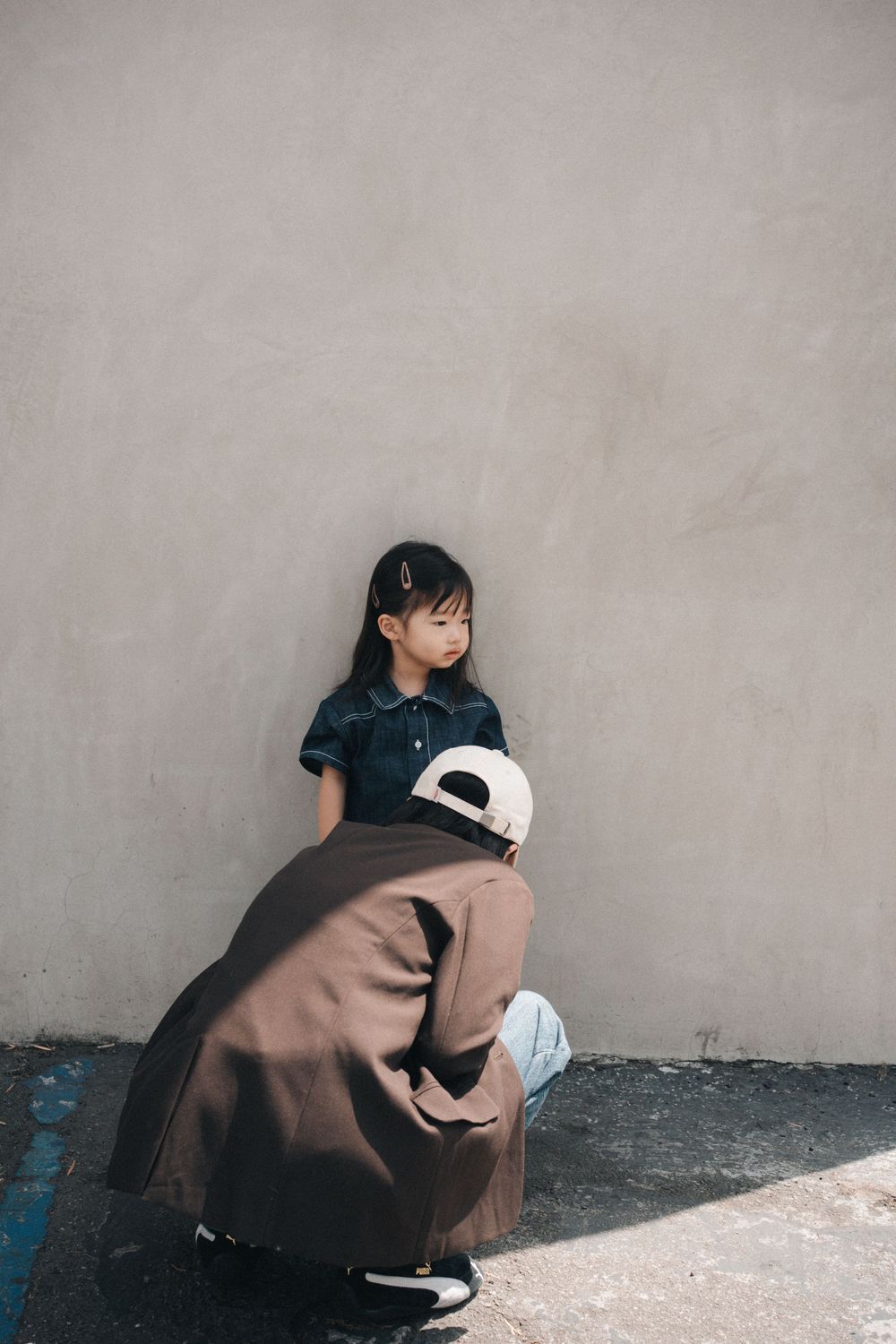 Two people in casual attire having a conversation against a beige wall in an urban setting.
