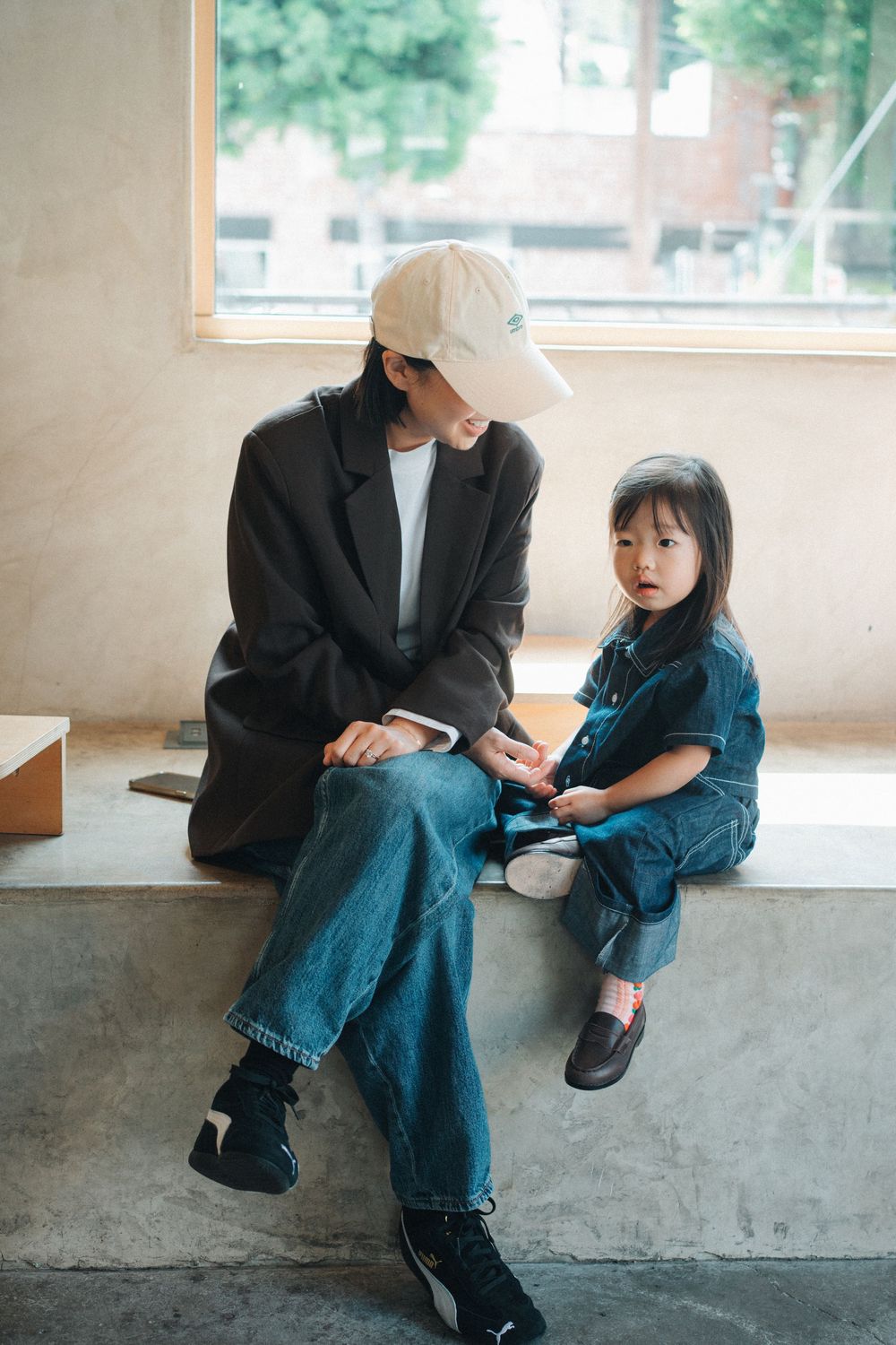 Modern casual outfits with black blazer and denim on concrete bench in natural window light.