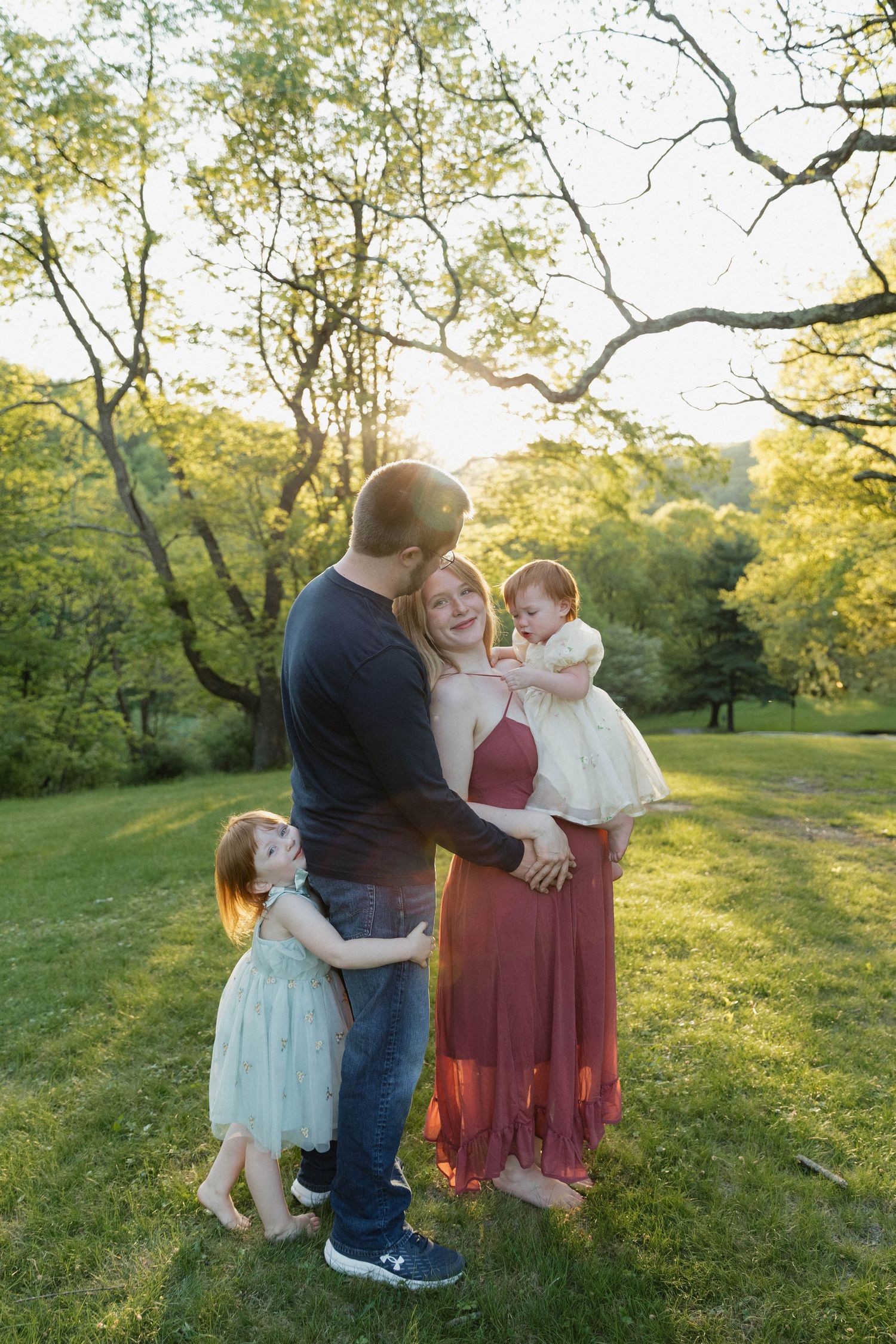 A tender moment shared between parent and child sitting together on grass at sunset with trees in background.