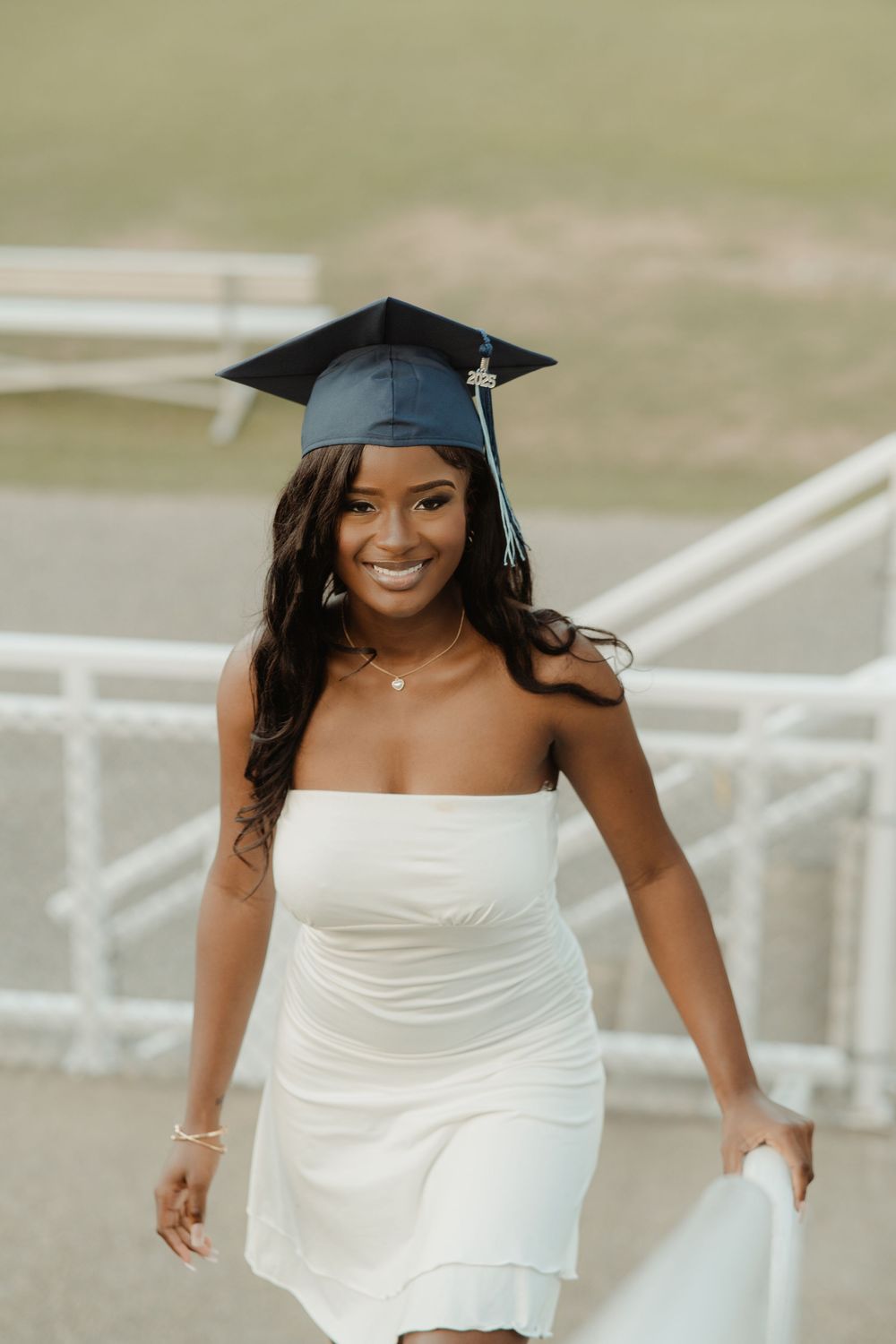 Graduate wearing a white dress and black cap celebrating their achievement with a bright smile.