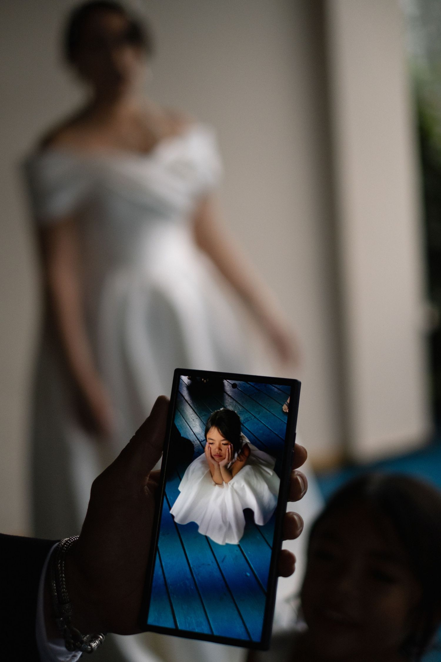 Someone in a white dress is captured in a wedding photo through a smartphone screen display in a creative composition.