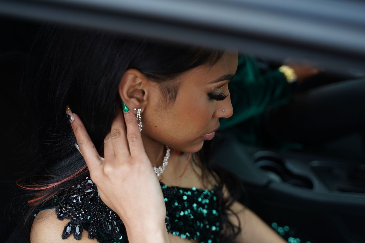 Woman wearing a black sequined dress adjusts her earring while sitting in a car.