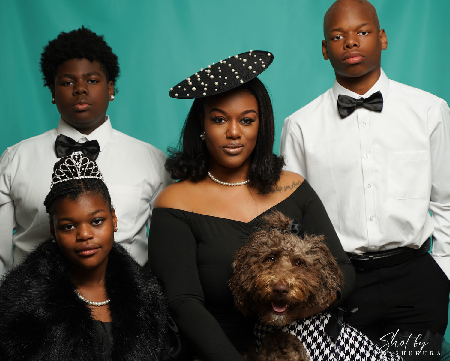 A stylish family portrait with matching black and white formal attire, hair accessories and a fluffy brown dog.