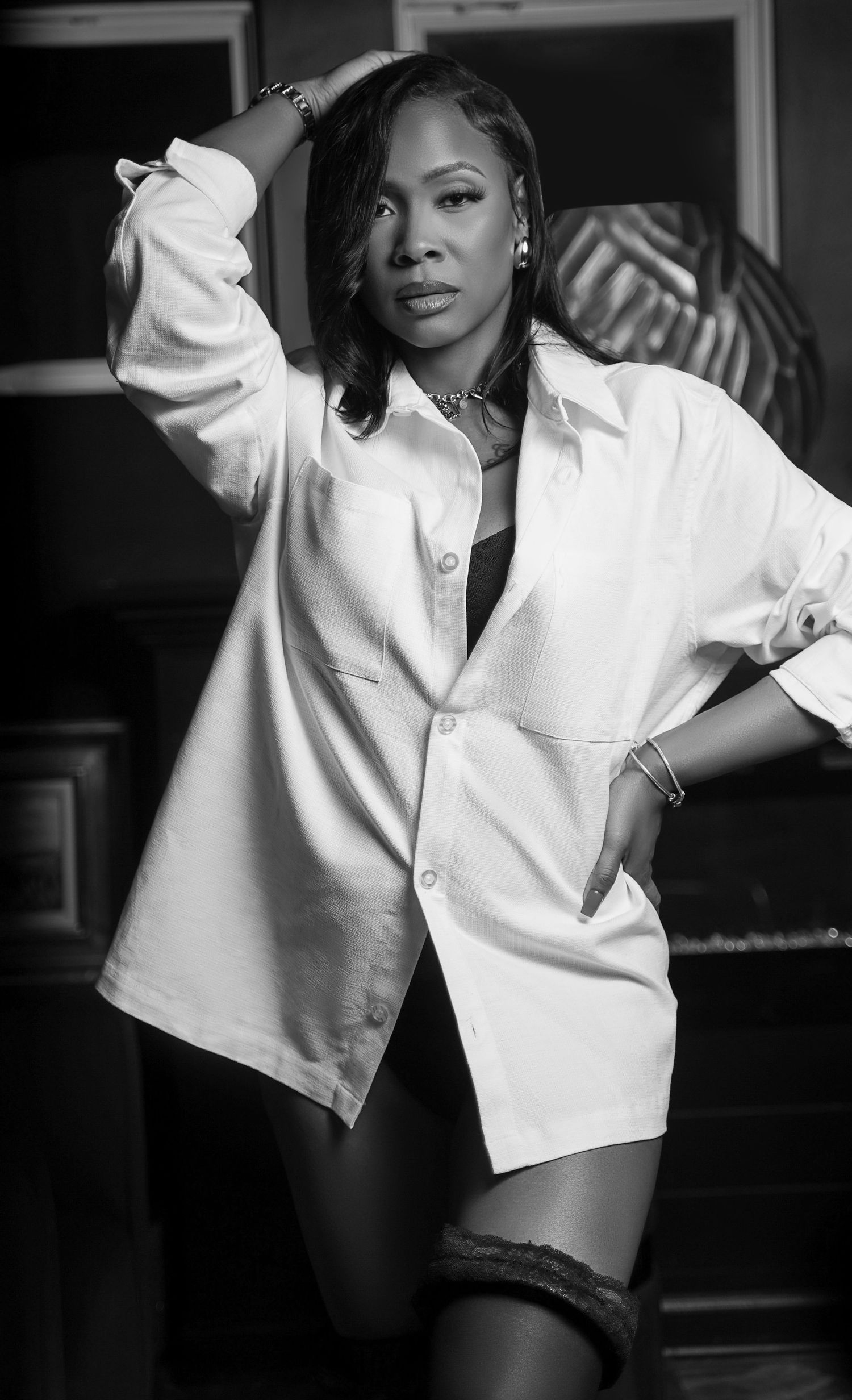 Black and white portrait of a person in oversized white button-up shirt with contemporary lighting against dark background.