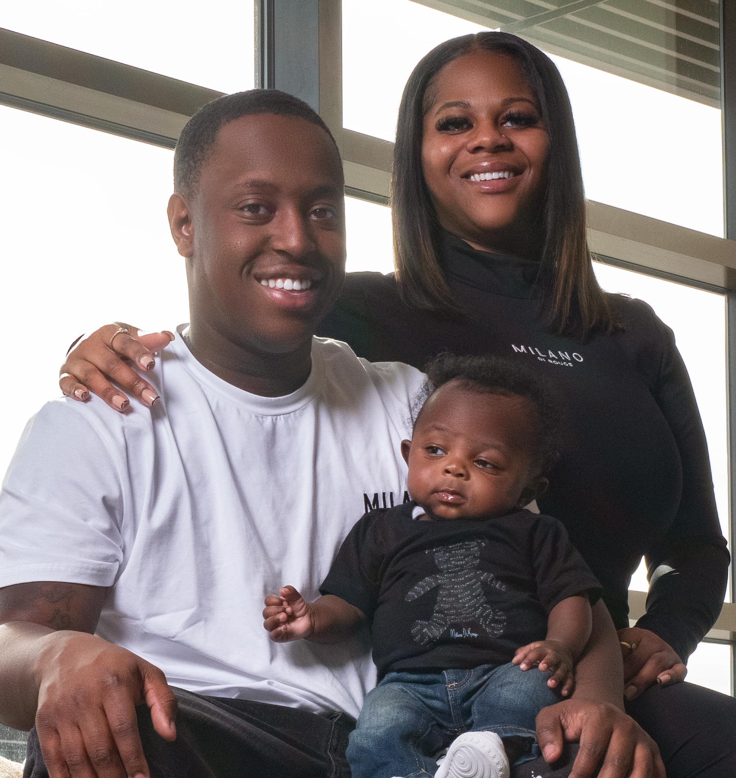 A loving family of three sits together indoors, wearing casual clothing and sharing a warm moment.