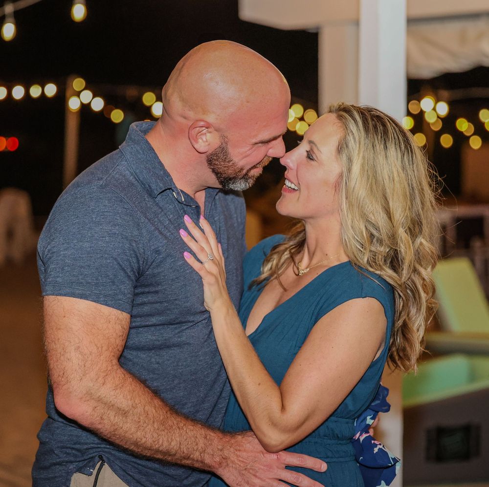 A couple shares an intimate moment while embracing under string lights at an evening celebration.