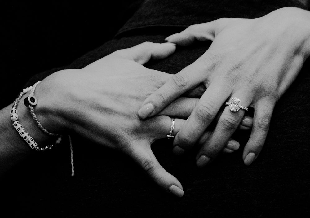 A black and white close-up photo of two hands with one placing a ring on the other, showing jewelry and a bracelet.