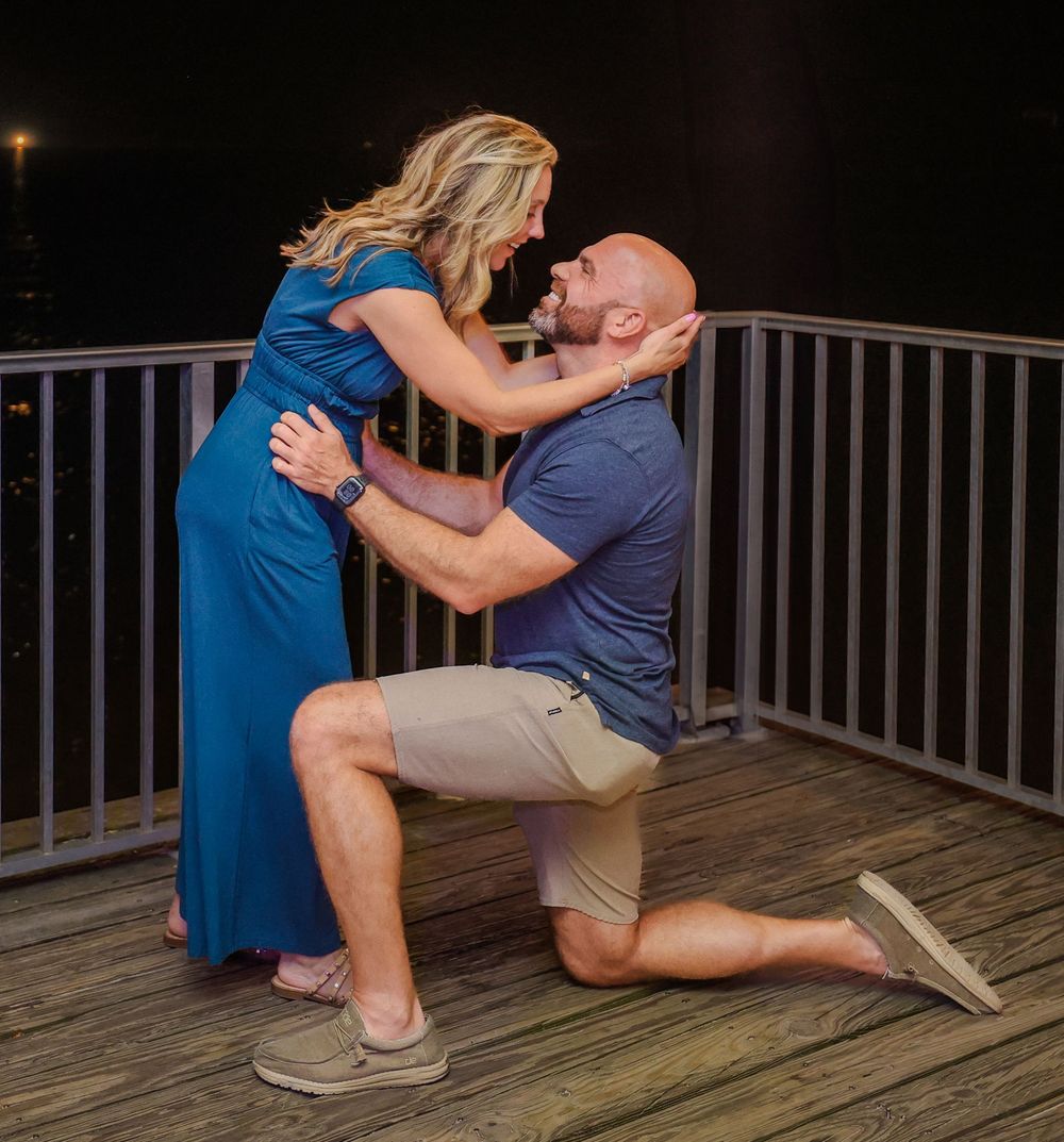 A couple embraces during a romantic proposal moment on a wooden deck at night.