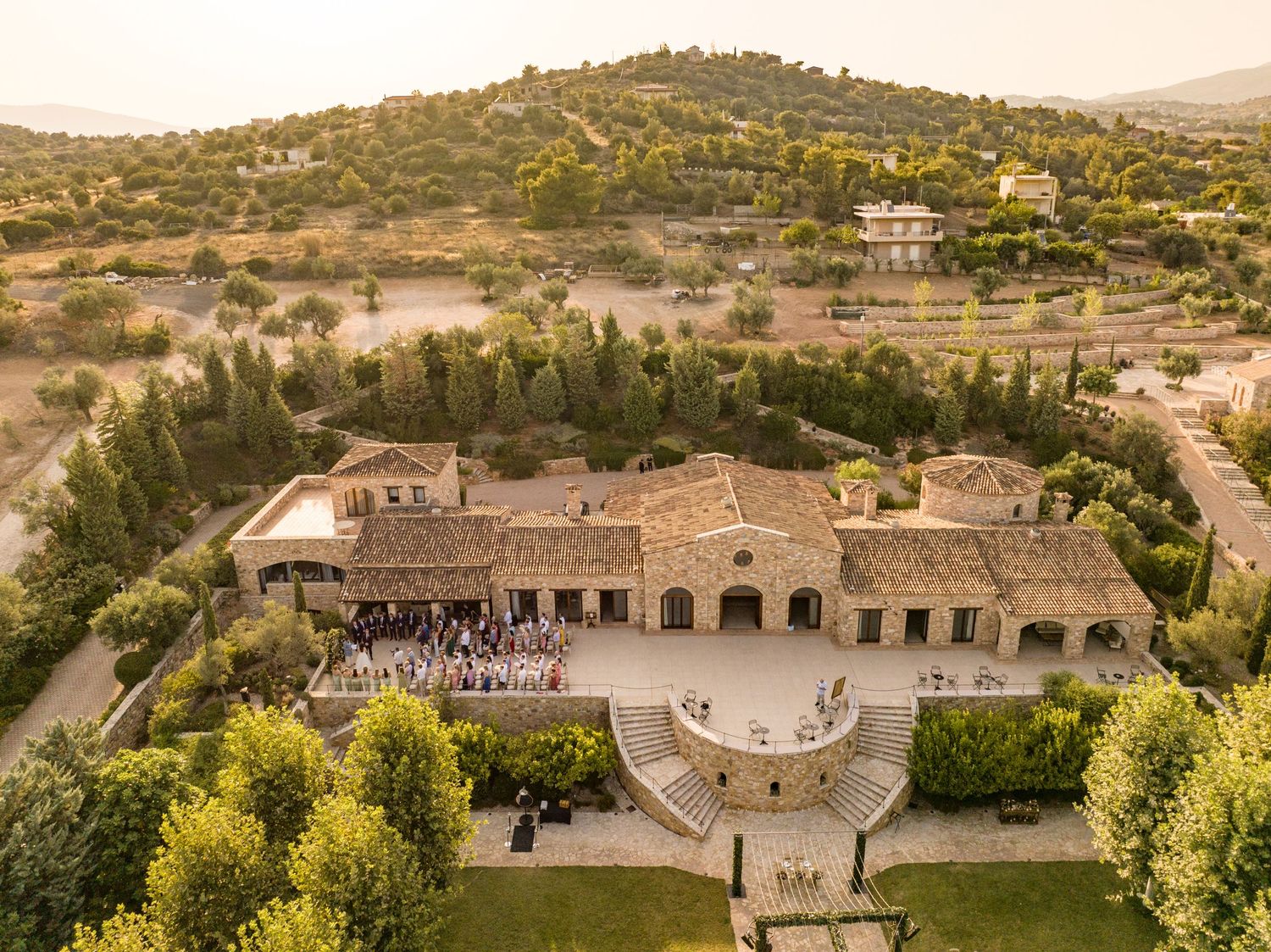 Aerial view of a luxury Mediterranean villa with stone courtyard and guests gathered outside.