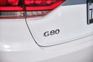 Close-up view of G80 emblem badge on the rear of a white luxury vehicle with taillights visible in frame.