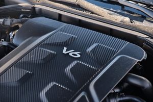 Close-up of a V6 engine cover with carbon fiber texture pattern and chrome badging.