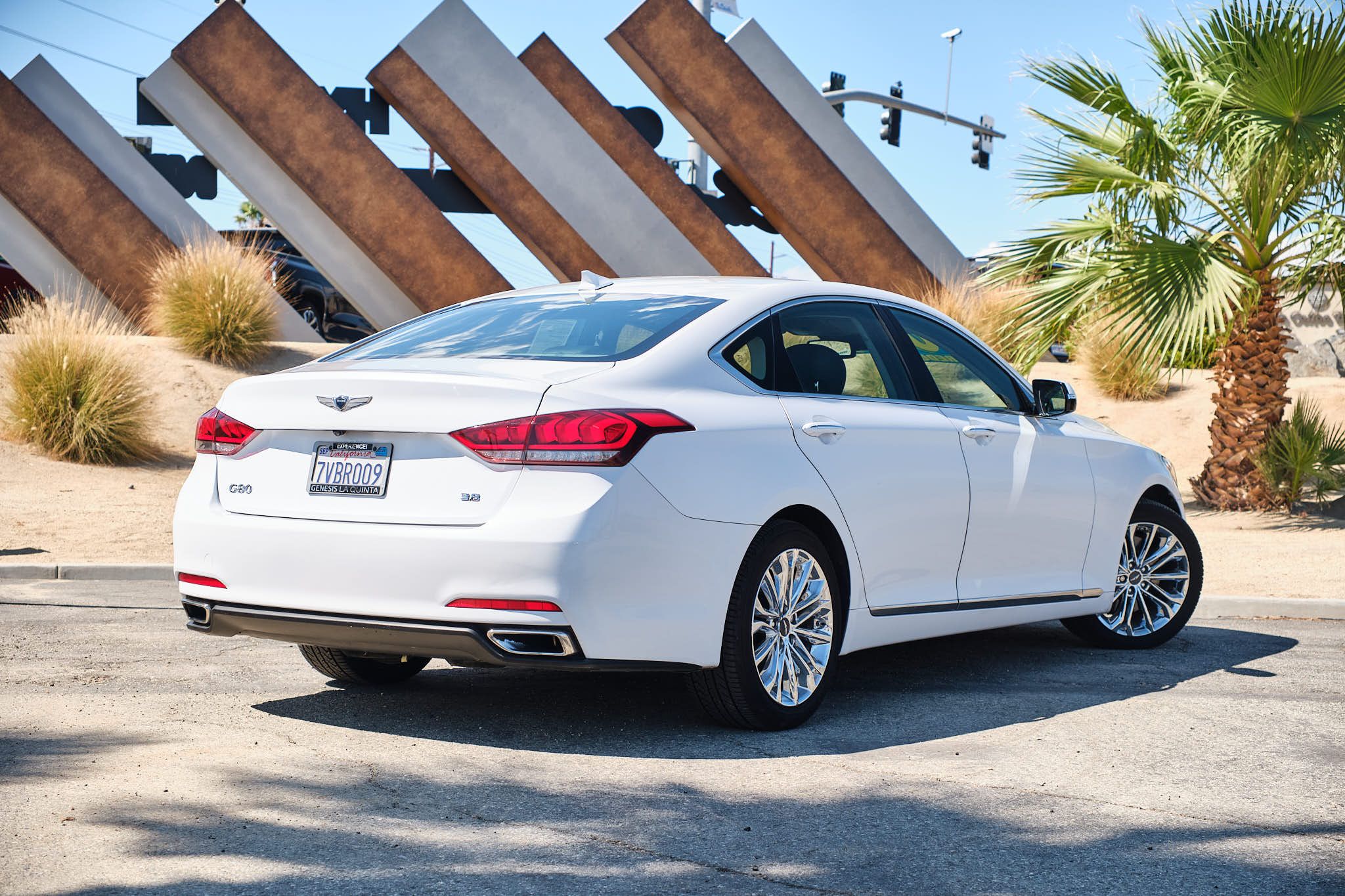 White Genesis luxury sedan rear view showcasing sleek design against modern architectural wall and palm trees.