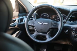 Interior view of a Hyundai Genesis luxury sedan steering wheel with winged badge logo and dashboard controls.