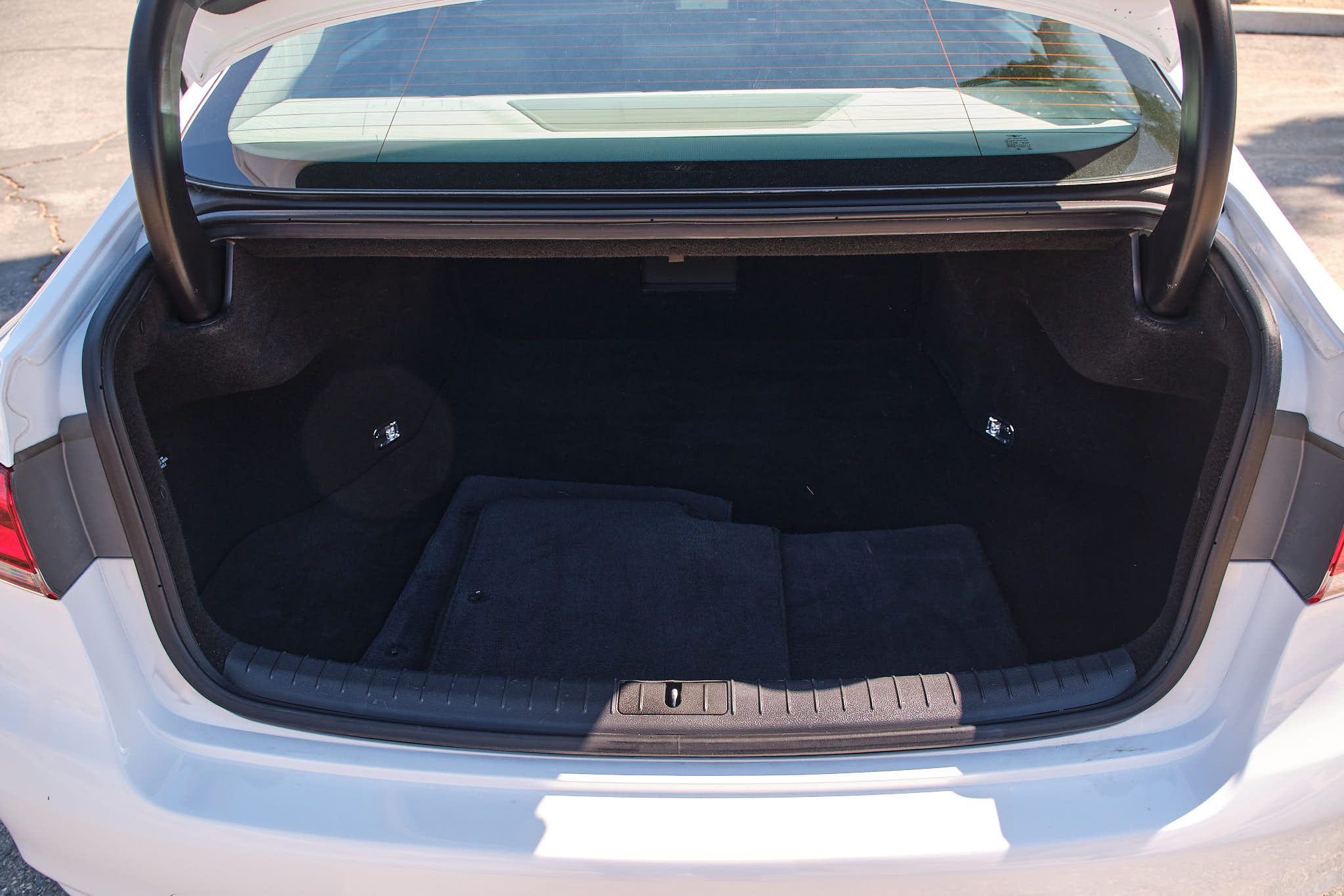 Open car trunk showing clean empty black carpeted cargo space of a sedan.