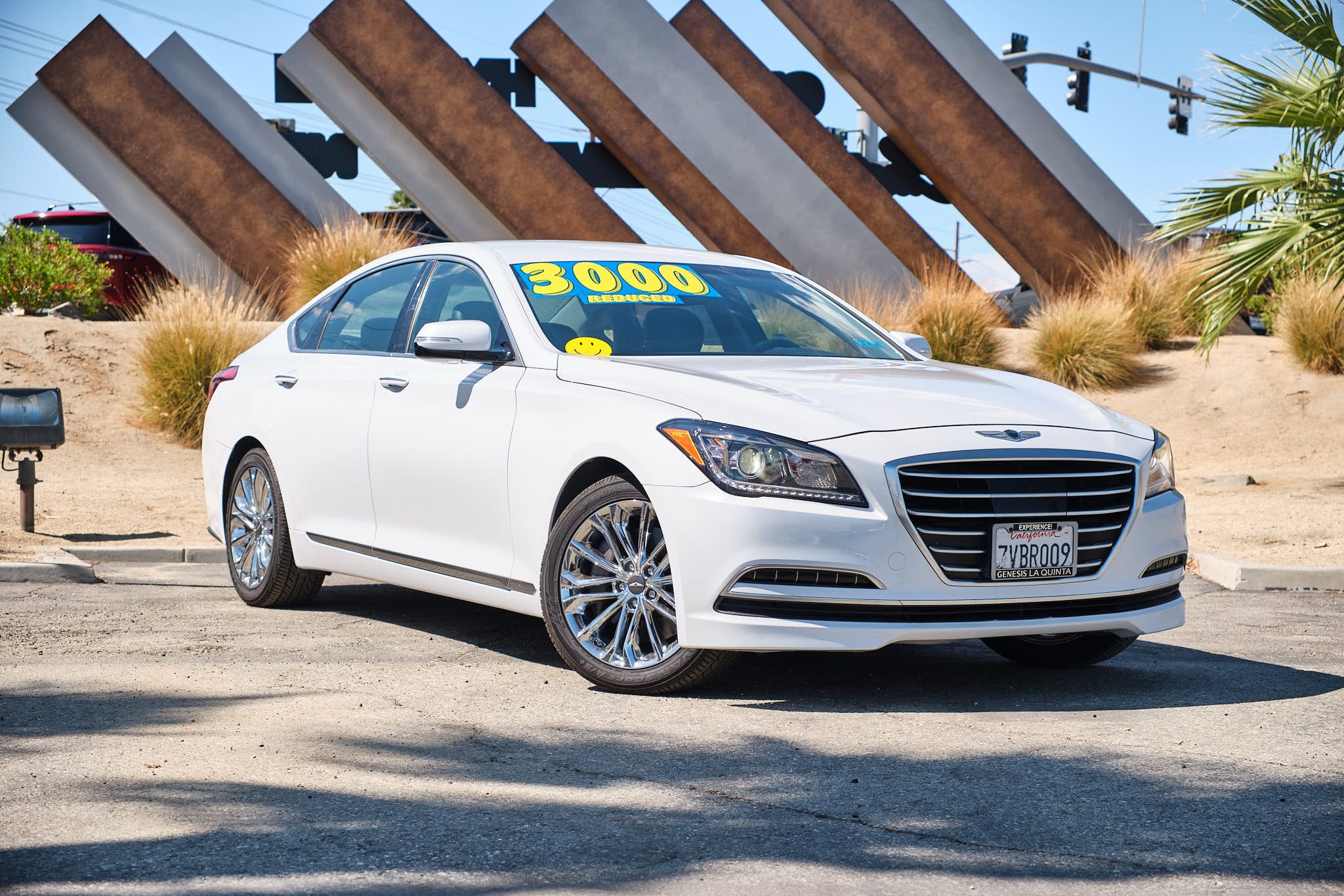 A white Hyundai Genesis luxury sedan parked in front of modern architectural elements with diagonal metal beams.