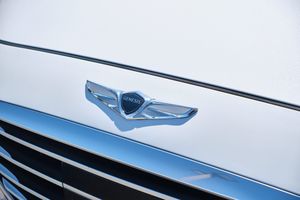 Close up of Genesis winged logo emblem in chrome against white car hood.