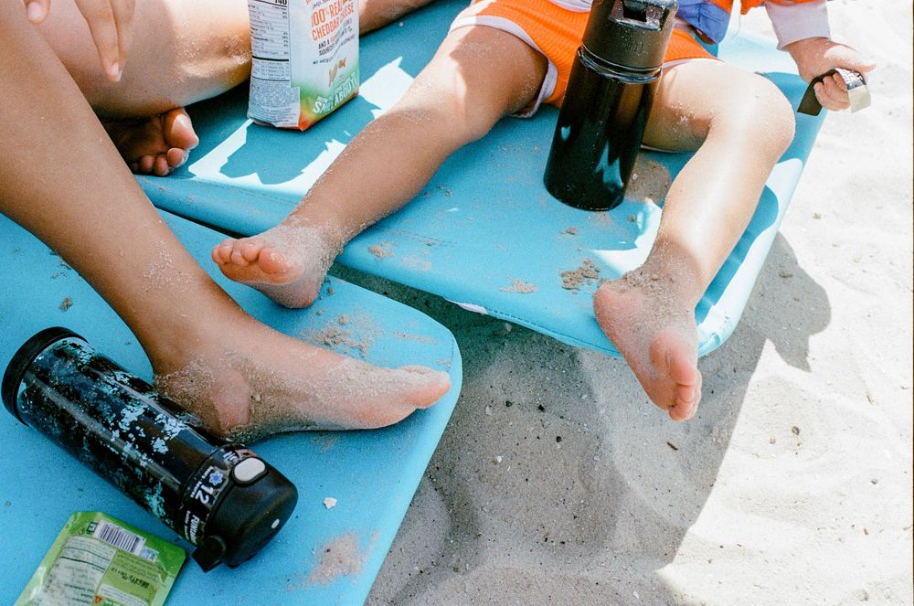 Two pairs of legs resting on a blue surface with sunscreen bottles and beach items scattered around.
