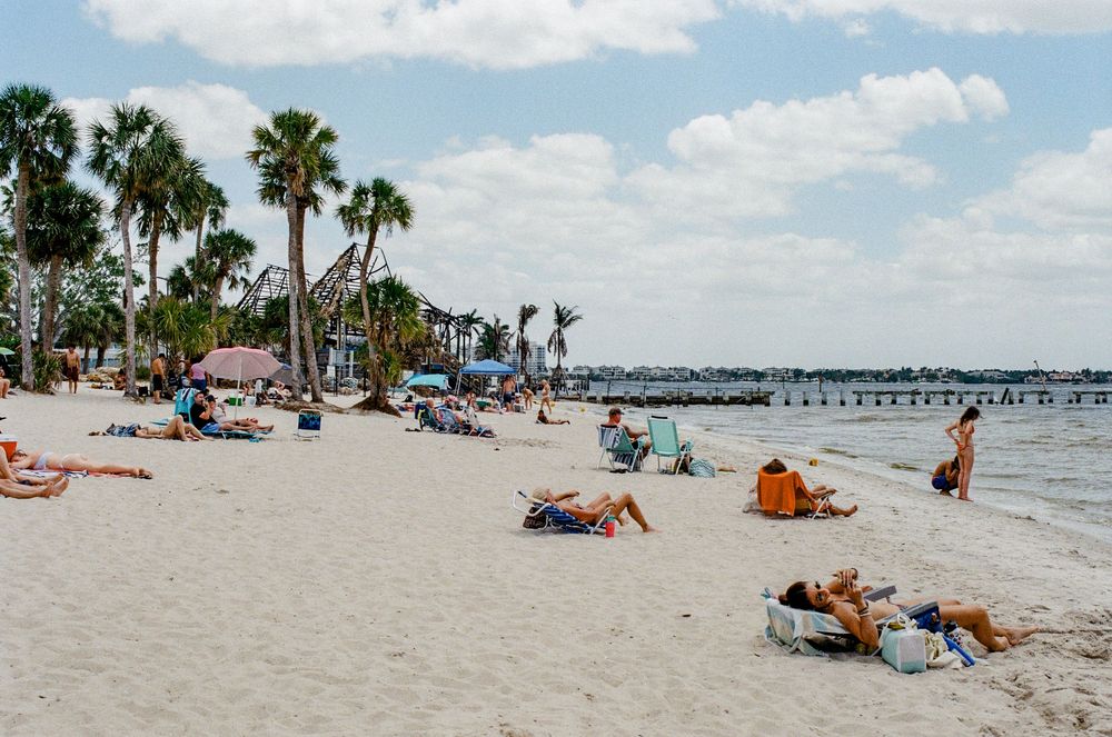 Beachgoers lounging on white sand with palm trees and a pier at a Florida beach.
