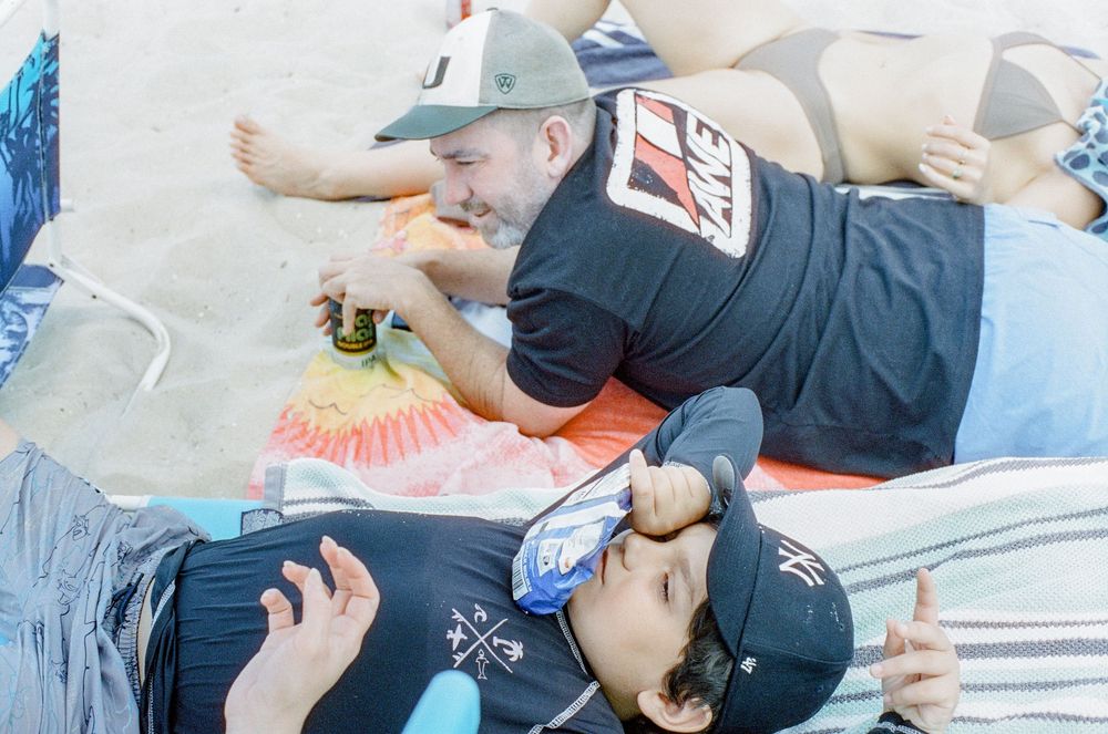 Two people recline on the ground at a festival while enjoying snacks and drinks in a relaxed summertime atmosphere.