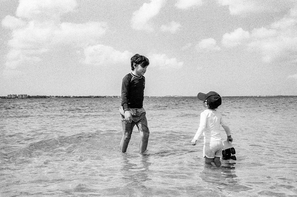 A black and white photo of people wading in shallow ocean water on a cloudy day.