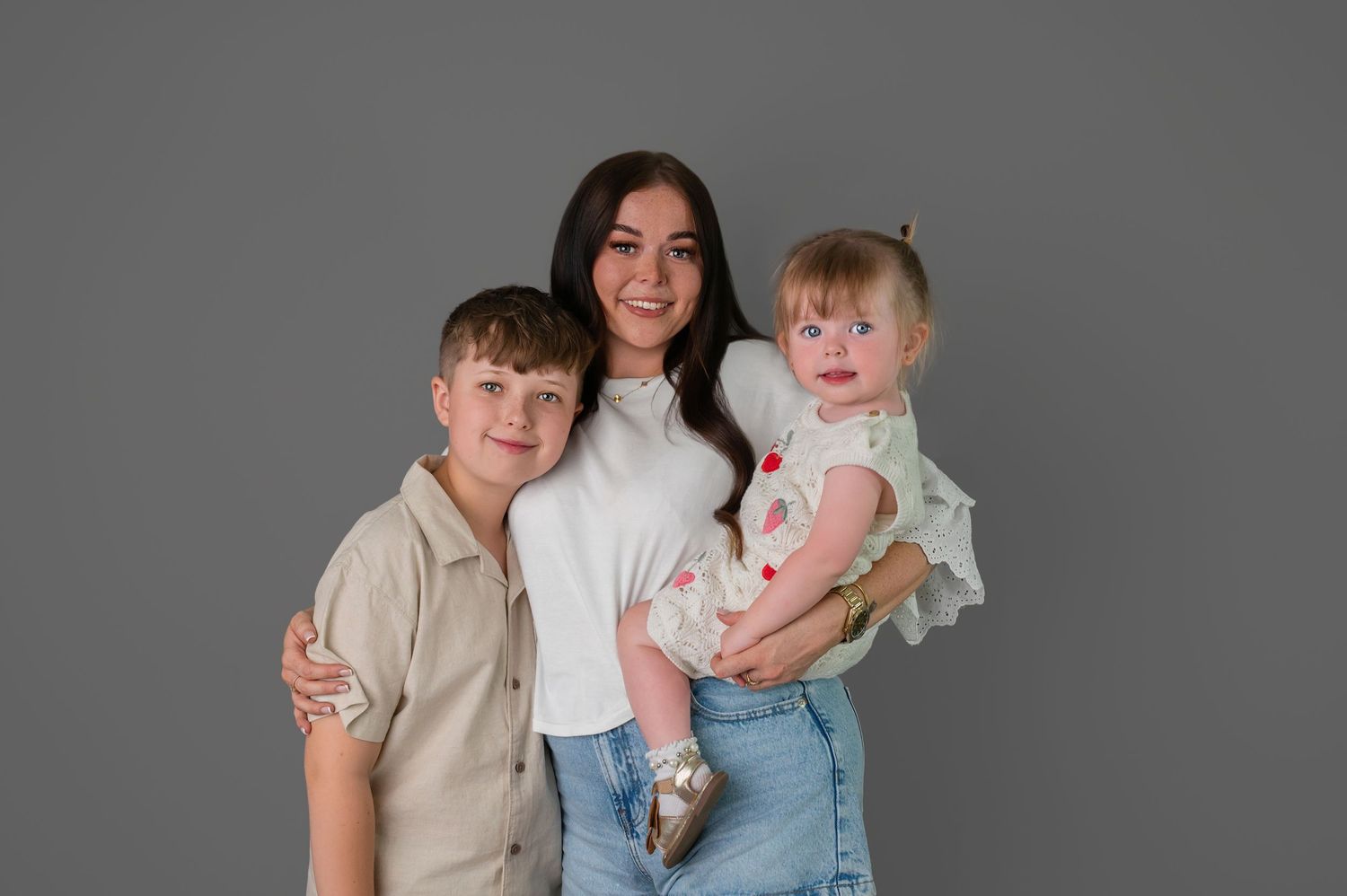 A family in coordinated red and white outfits poses together against a gray studio backdrop.