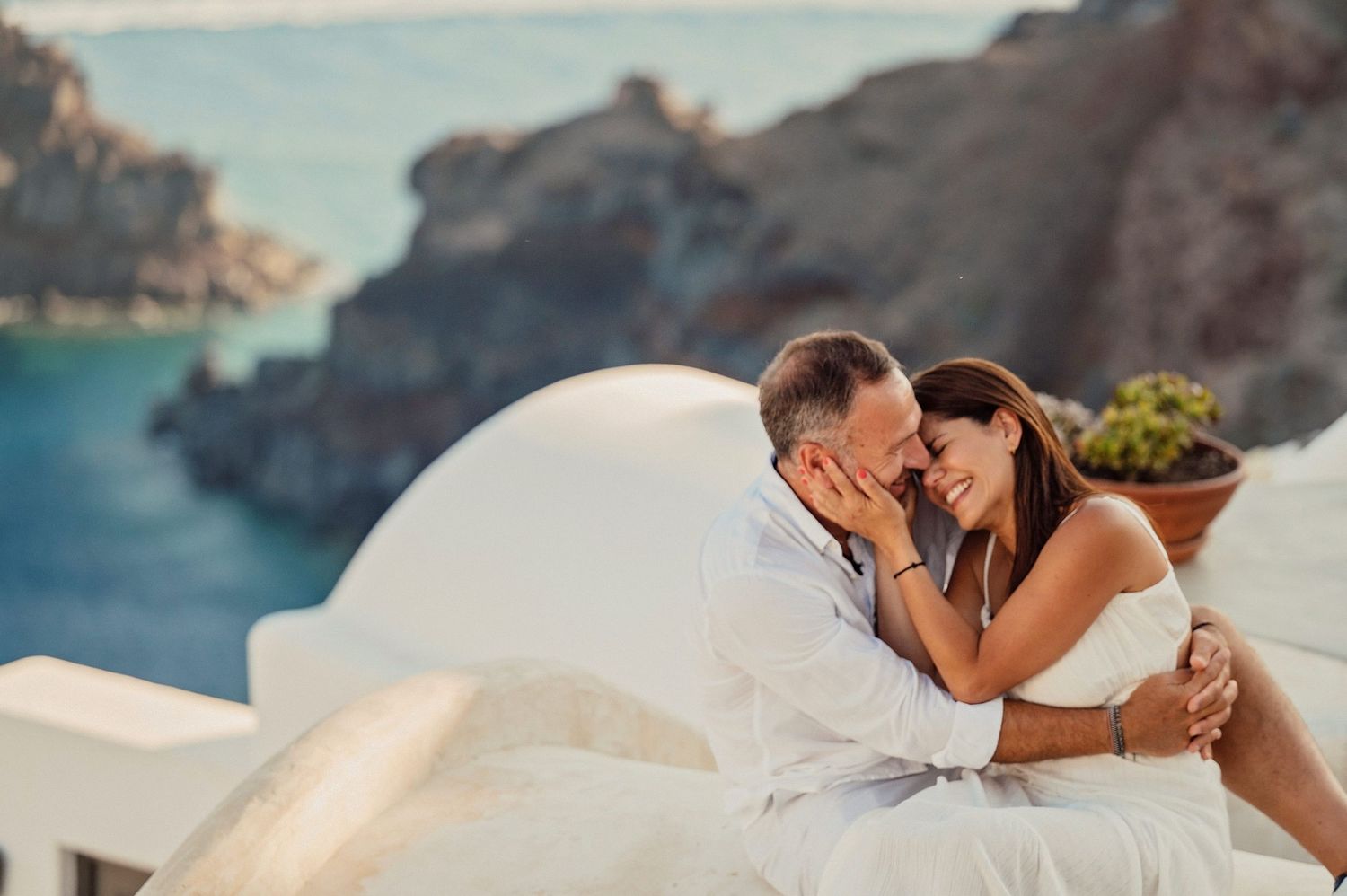 Romantic couple in white embracing on white dome structure overlooking Mediterranean sea.