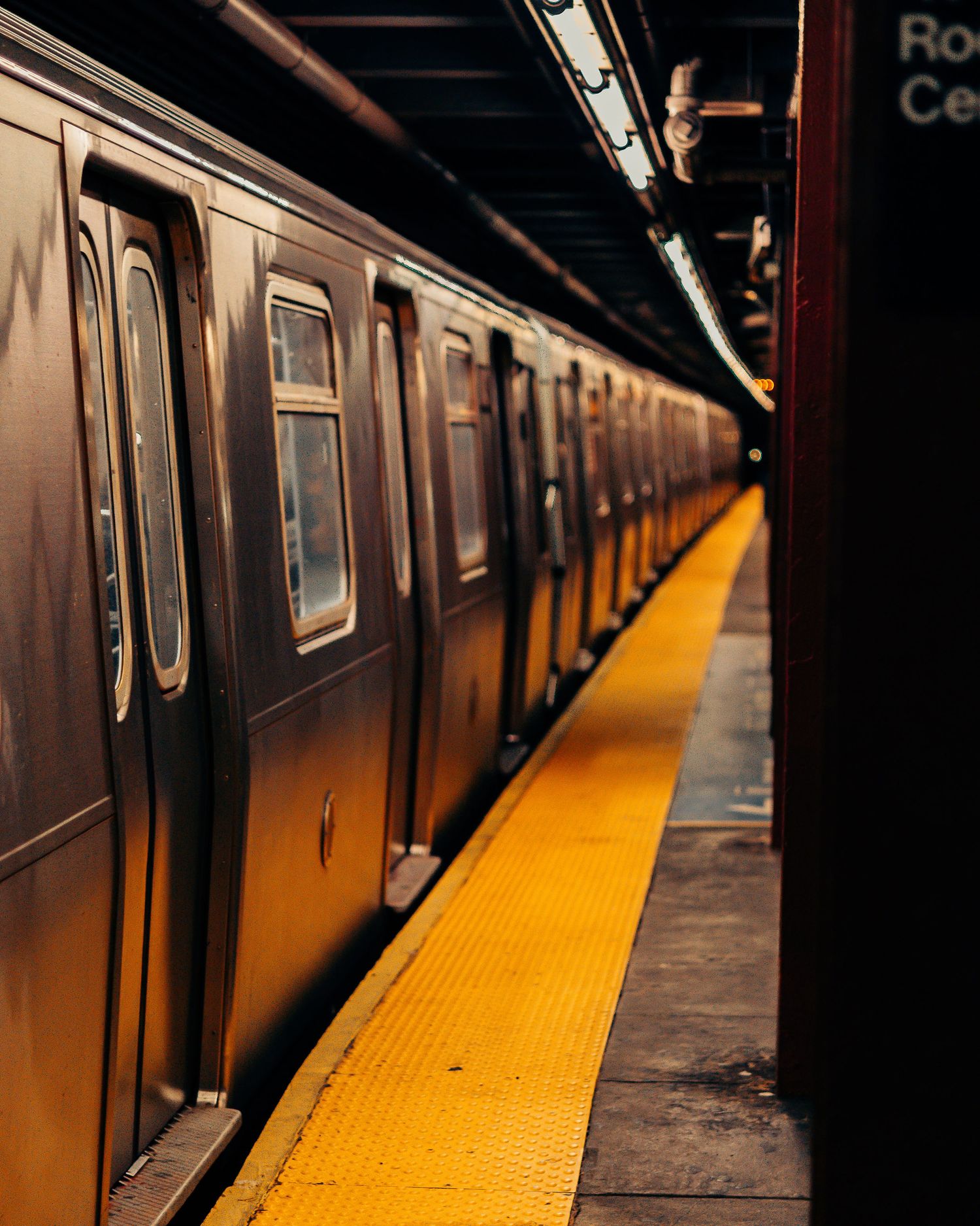 Subway train car at platform with distinctive yellow safety strip in dark underground station.