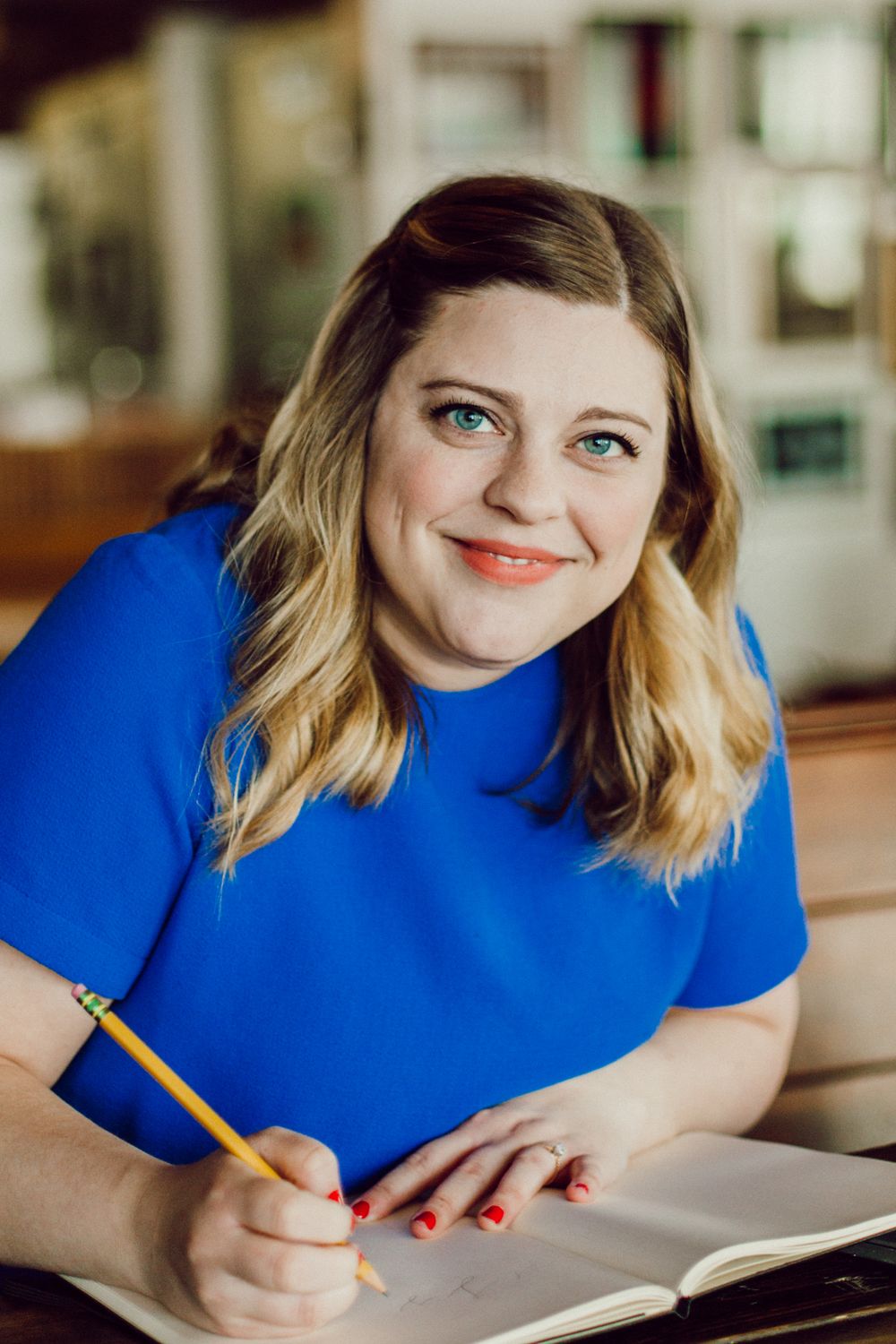 A person in bright blue writes in a notebook while seated at a desk.