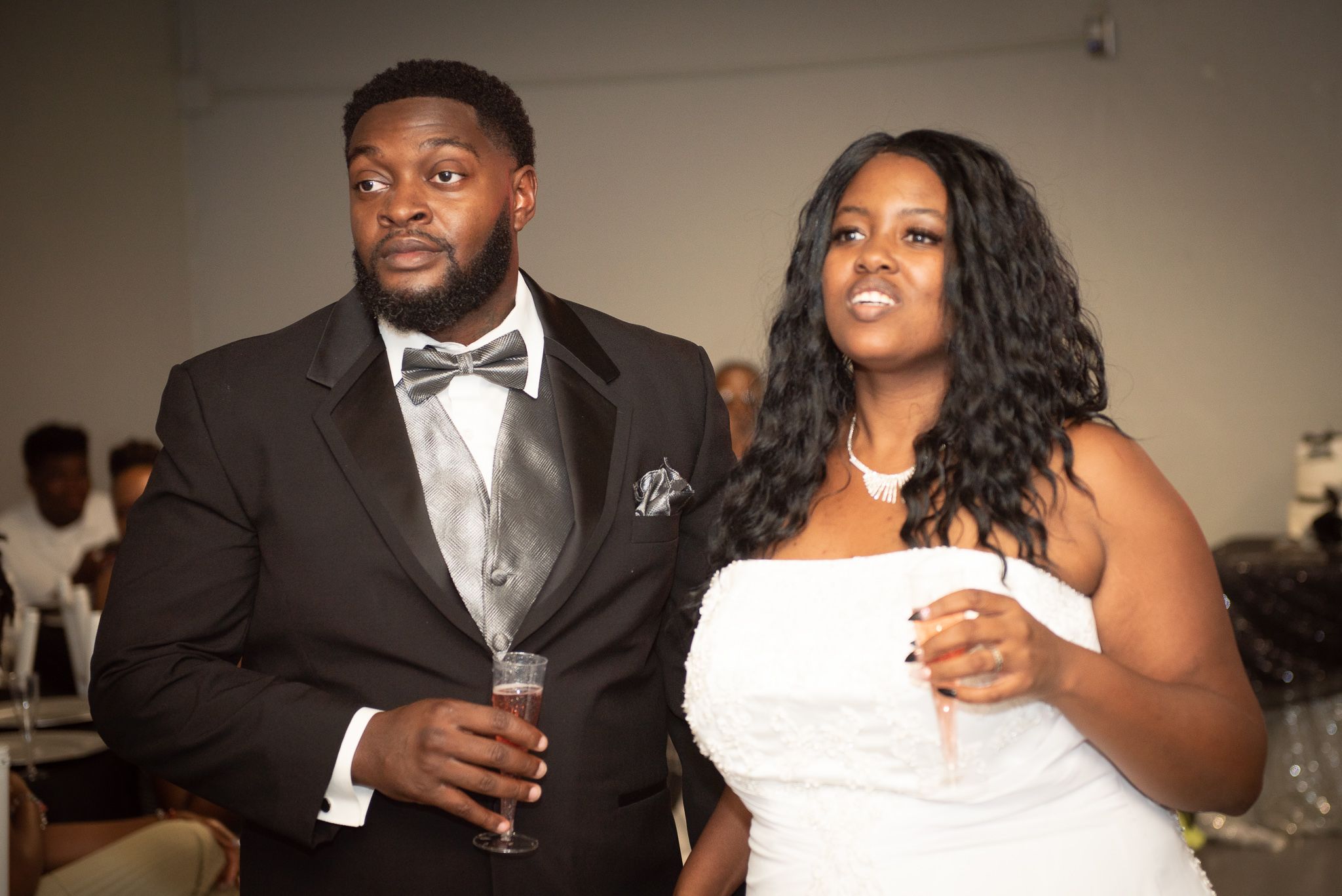 A couple in formal attire smiles while holding drinks at an elegant event.