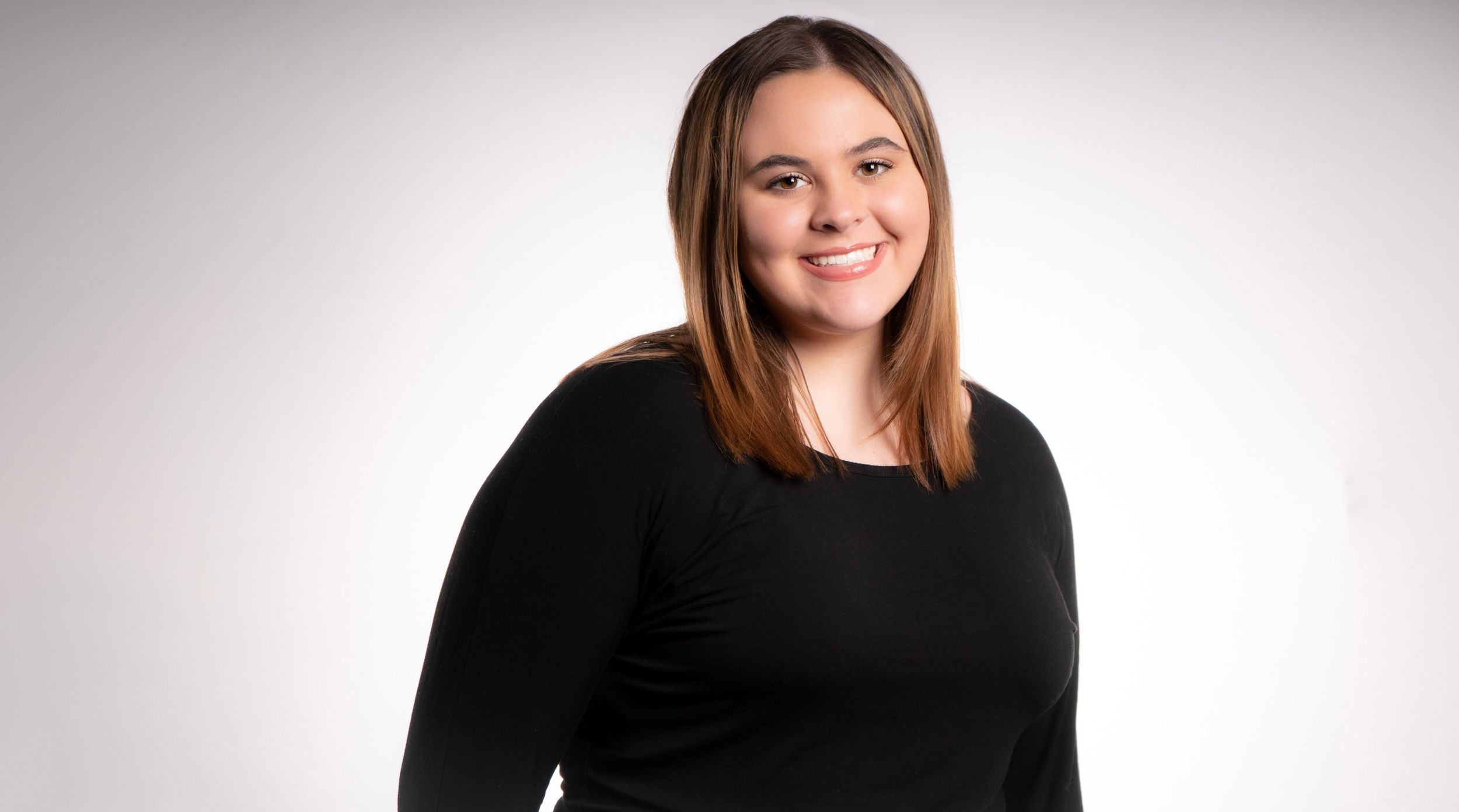 Professional studio portrait with a black long-sleeved top against a light gray gradient background.